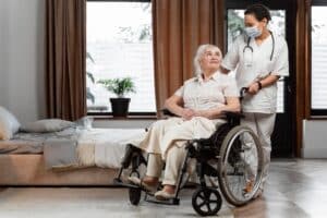 Nurse assisting an elderly woman in a wheelchair inside a nursing home.