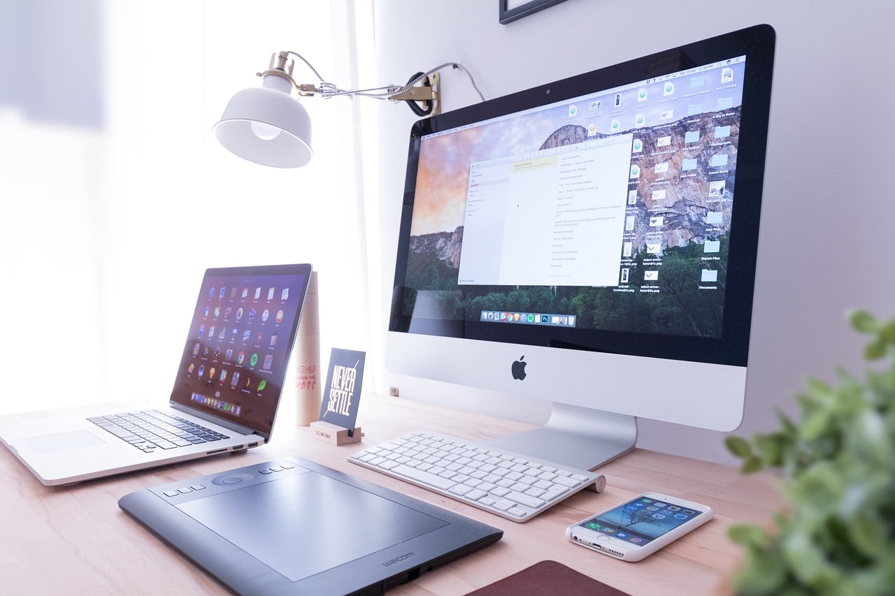 a laptop, Apple PC, and other devices on a table